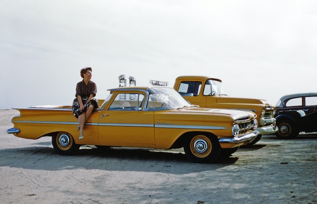 Woman sits on top of a yellow vintage car.
