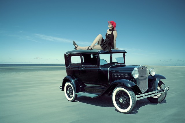 A woman donned in typical flapper fashion atop a vintage vehicle. 