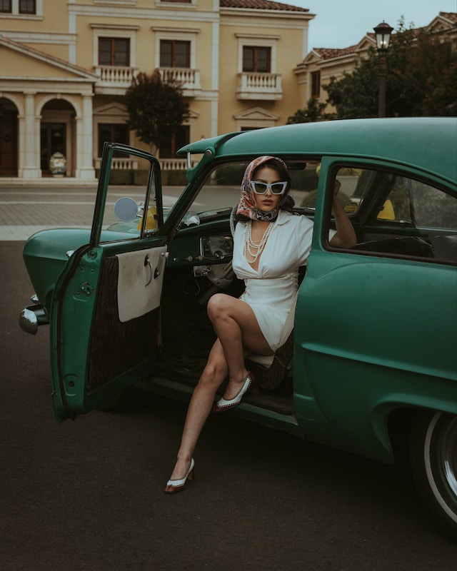 Woman in white dress stepping out of a green vintage car.