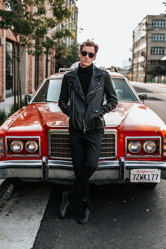 Man in black poses on a red vintage car